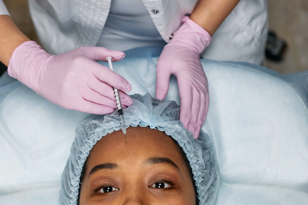 Xeomin vs Botox is pictured as a woman who is in blue scrubs gets injectables into her forehead.